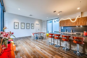 A modern kitchen with a bar area, wooden flooring, and framed artwork on the walls. - StayAU Bulleen Urban Hideaway 5BR (Bulleen)