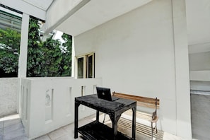 A room with a white wall, a wooden bench, and a small table with a laptop. - Hotel O Near Ciputra World Surabaya Formerly Darmo Residence (Surabaya)