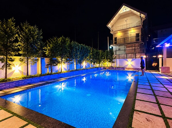 A nighttime swimming pool area with a two-story building in the background.