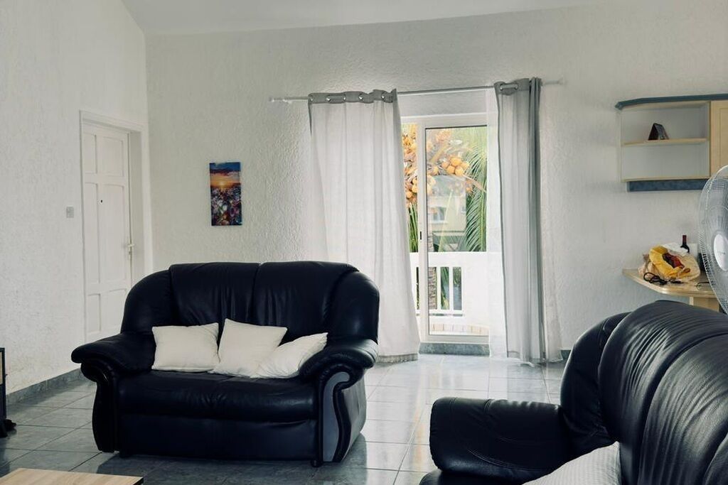 Een woonkamer met een zwarte leren bank, een witte deur, een schilderij aan de muur en een uitzicht door een glazen deur.