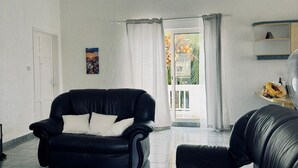 Un soggiorno con un divano in pelle nera, una porta bianca, un quadro appeso al muro e vista all'esterno attraverso una porta vetrata.