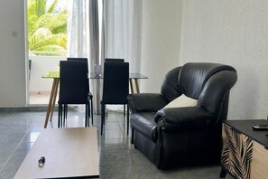 A modern living room with a leather sofa, a glass table, and chairs. - Blue Water Retreat – Cozy 1-Bedroom Stay Near Flic en Flac Beach (Flic en Flac)