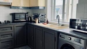Una cucina con mobili scuri, un forno a microonde, un tostapane, un lavello e una lavatrice.