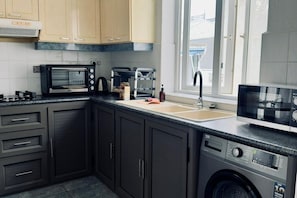Una cocina con armarios oscuros, un microondas, un tostador, un lavabo y una lavadora.