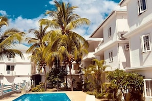 Zona de piscina con palmeras, un edificio blanco y cielo despejado.