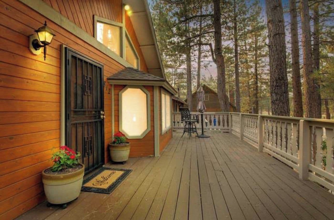 Une terrasse en bois avec une rambarde, des plantes en pot et une porte surmontée d’une fenêtre.