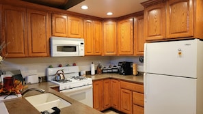 A kitchen with wooden cabinets, a white stove, a microwave, and a refrigerator. - Big Bear Cozy Cabin • Hot Tub • Family Friendly (Big Bear)