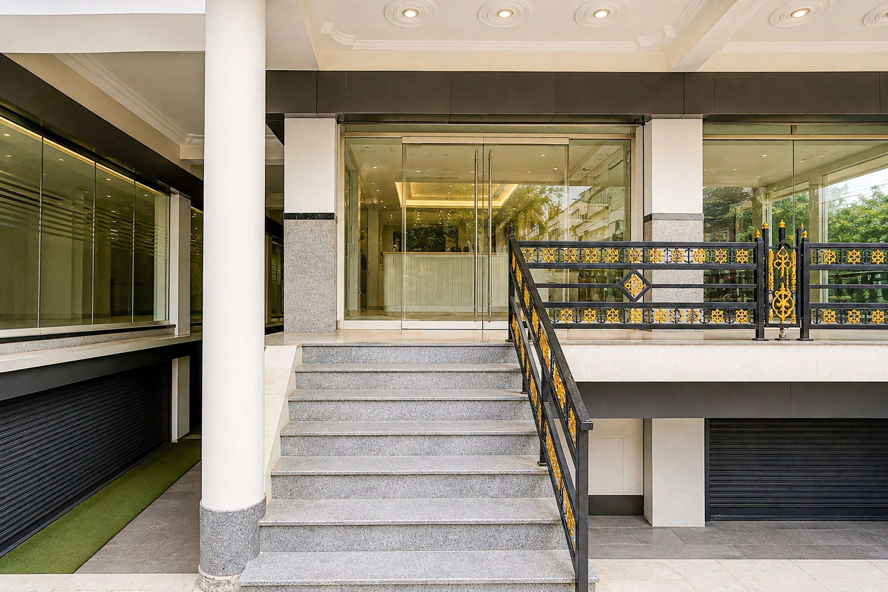 A modern building entrance with a glass door, a staircase with a metal railing, and a view of the street outside.