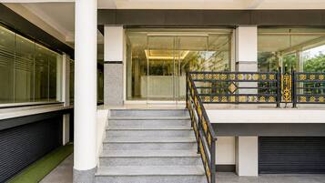A modern building entrance with a glass door, a staircase with a metal railing, and a view of the street outside.