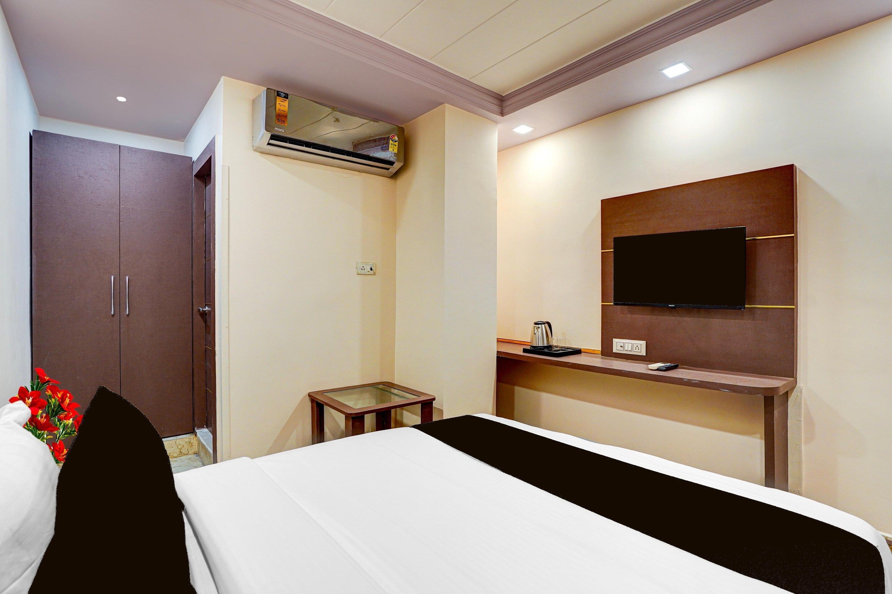 A hotel room with a bed, a TV mounted on the wall, a small table, and a wardrobe.