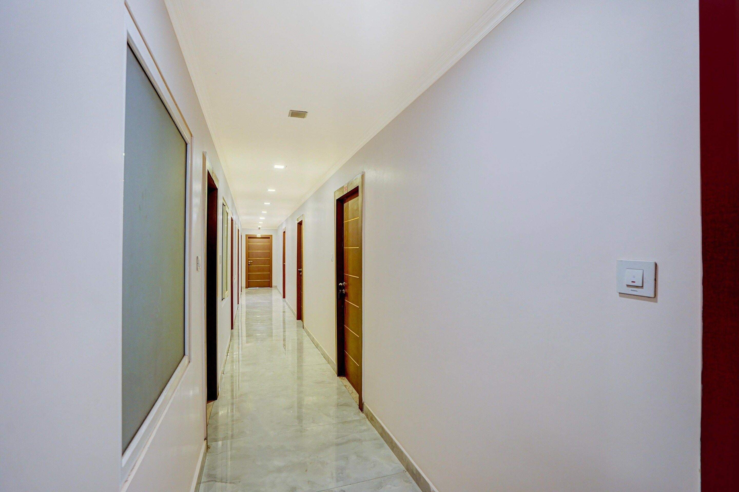 A corridor with doors on both sides, a tiled floor, and a ceiling with recessed lighting.
