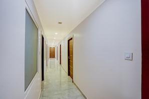 Un pasillo con puertas a ambos lados, suelo de baldosas e iluminación empotrada en el techo.