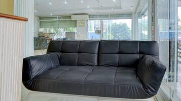 A black leather sofa in a modern room with a large window, a clock on the wall, and a ceiling with recessed lighting.