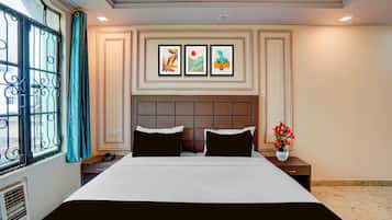 A hotel room with a bed, two pillows, a nightstand, a phone, a vase with flowers, and three framed pictures on the wall.