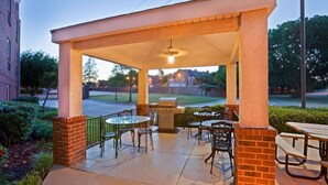 Ein überdachter Patio-Bereich mit Grill, Tischen und Stühlen.