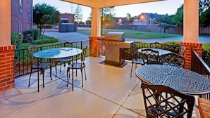 Eine Terrasse im Freien mit Grill, Tischen und Stühlen.