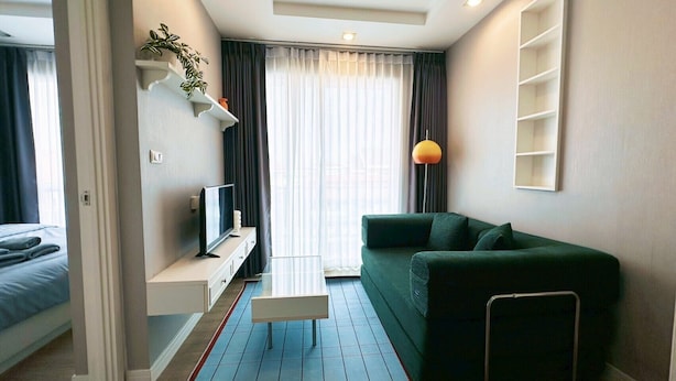A modern hotel room with a bed, a TV on a white console, a green sofa, and a window with curtains. - Relax, Stay and Enjoy Bangsean. Nearby Attractions & Amenities. (Tambon Saen Suk)