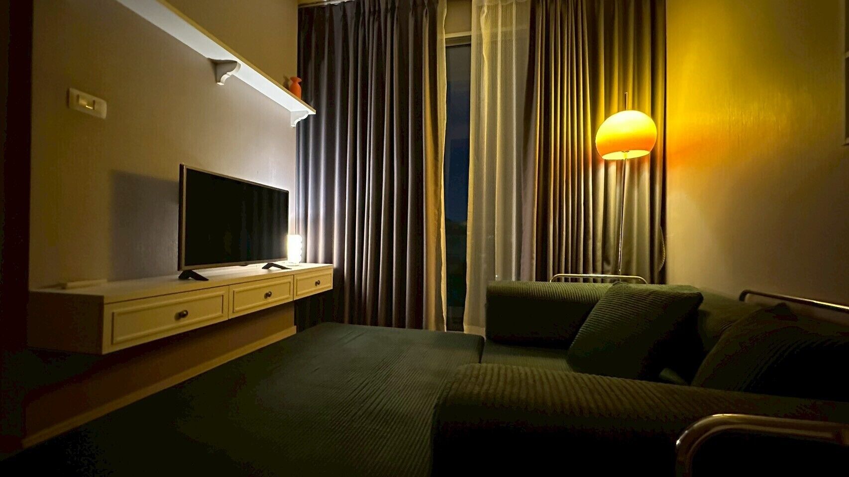 Ett hotellrum med en säng, en tv på ett stativ, ett nattduksbord och en lampa.