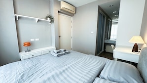 A hotel room with a bed, bedside table, lamp, and a wardrobe. - Relax, Stay and Enjoy Bangsean. Nearby Attractions & Amenities. (Tambon Saen Suk)