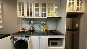 A compact kitchenette with a washing machine, microwave, and a stove.