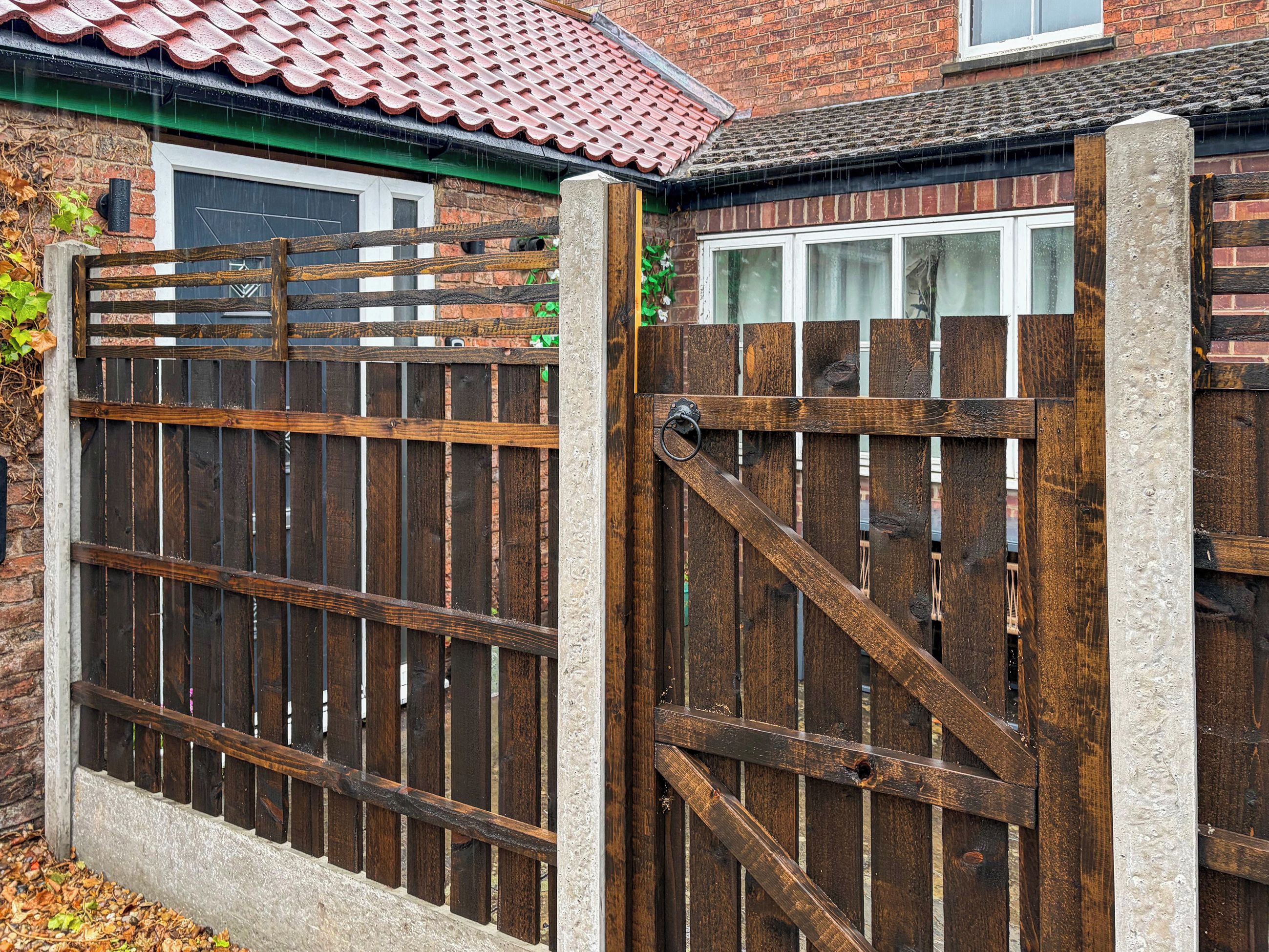 A wooden gate with a metal latch, set in a brick wall with a tiled roof.