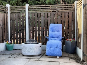 Un espace patio avec un fauteuil bleu rembourré, un chauffage d’extérieur rond et une clôture en bois.