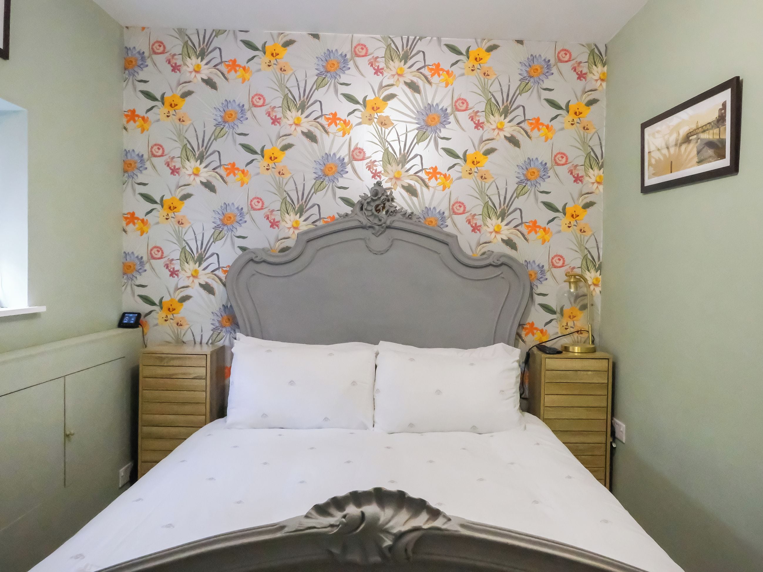 A bed with a grey headboard, two bedside tables, and a floral wallpaper pattern.