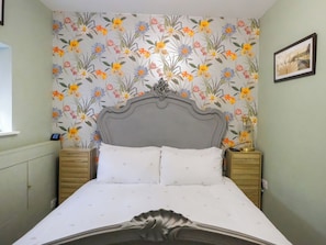 Un lit avec une tête de lit grise, deux tables de chevet et un papier peint à motifs floraux.