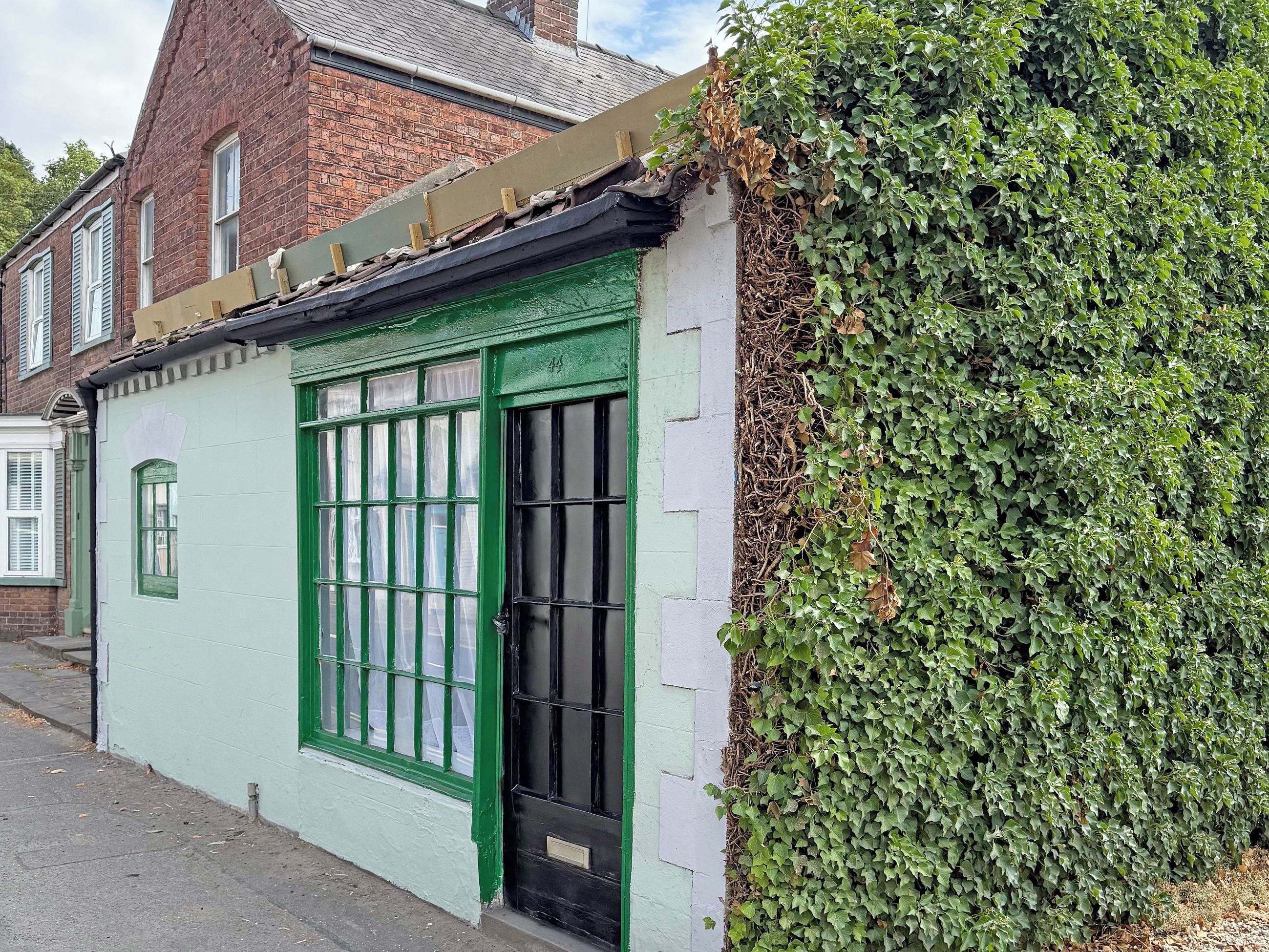 A building with a green door and windows, adjacent to a hedge.