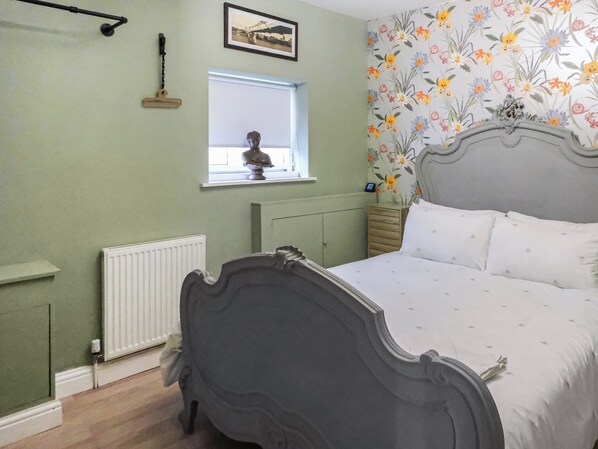 A bedroom with a bed, a radiator, a window with a statue, and floral wallpaper.