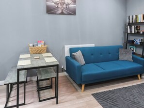 A living room with a blue sofa, a small table, a basket, and a bookshelf.