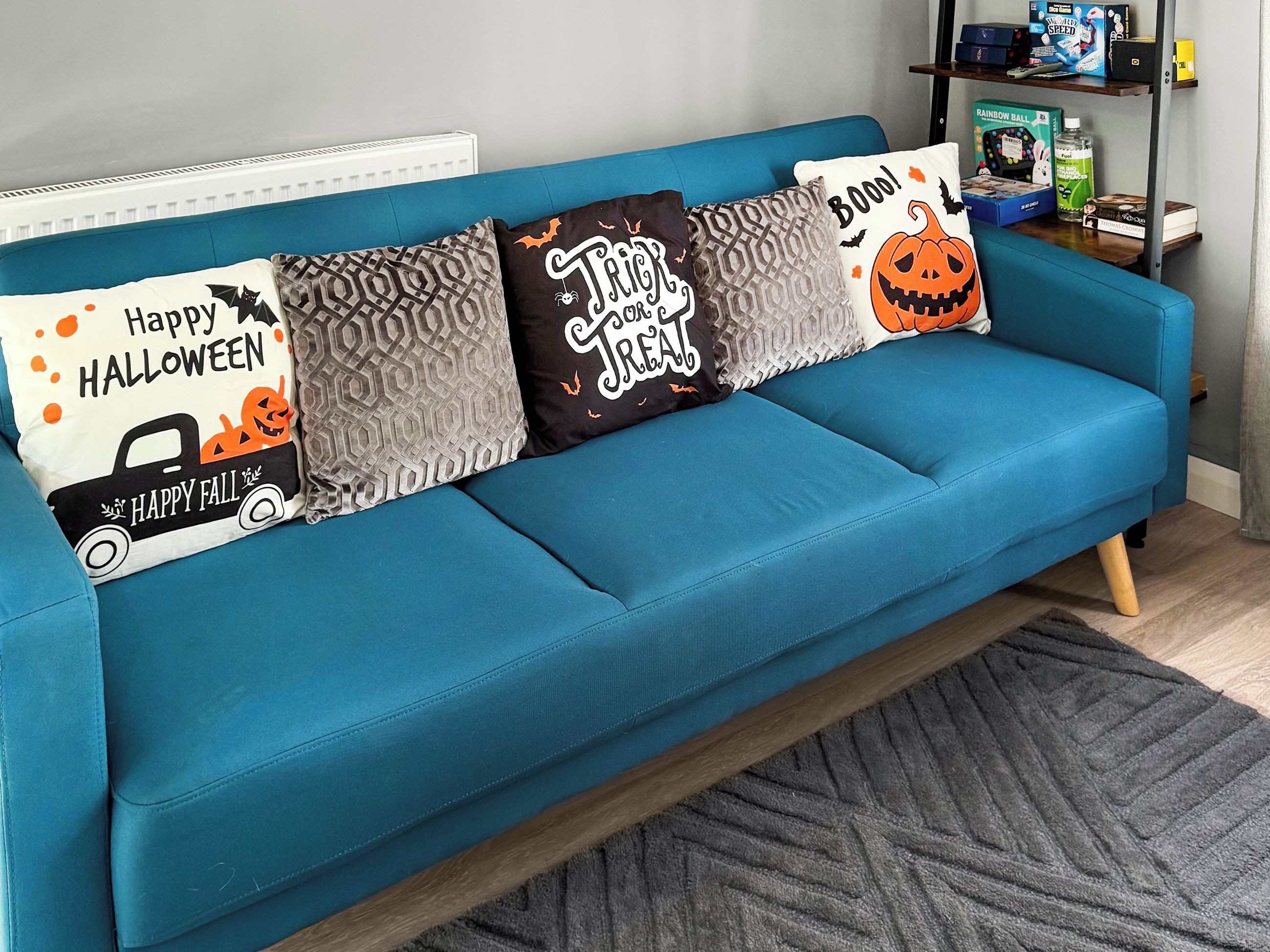 Un canapé de couleur turquoise agrémenté de quatre coussins décoratifs, chacun orné d’un motif et d’un texte sur le thème d’Halloween.