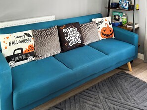 Un canapé de couleur turquoise agrémenté de quatre coussins décoratifs, chacun orné d’un motif et d’un texte sur le thème d’Halloween.