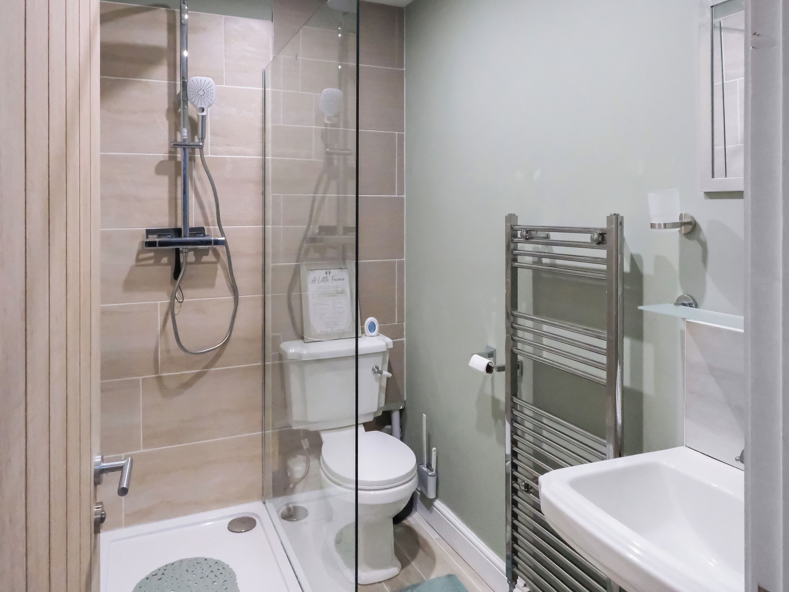 Un baño moderno con ducha envuelta en cristal, inodoro y lavamanos blanco.