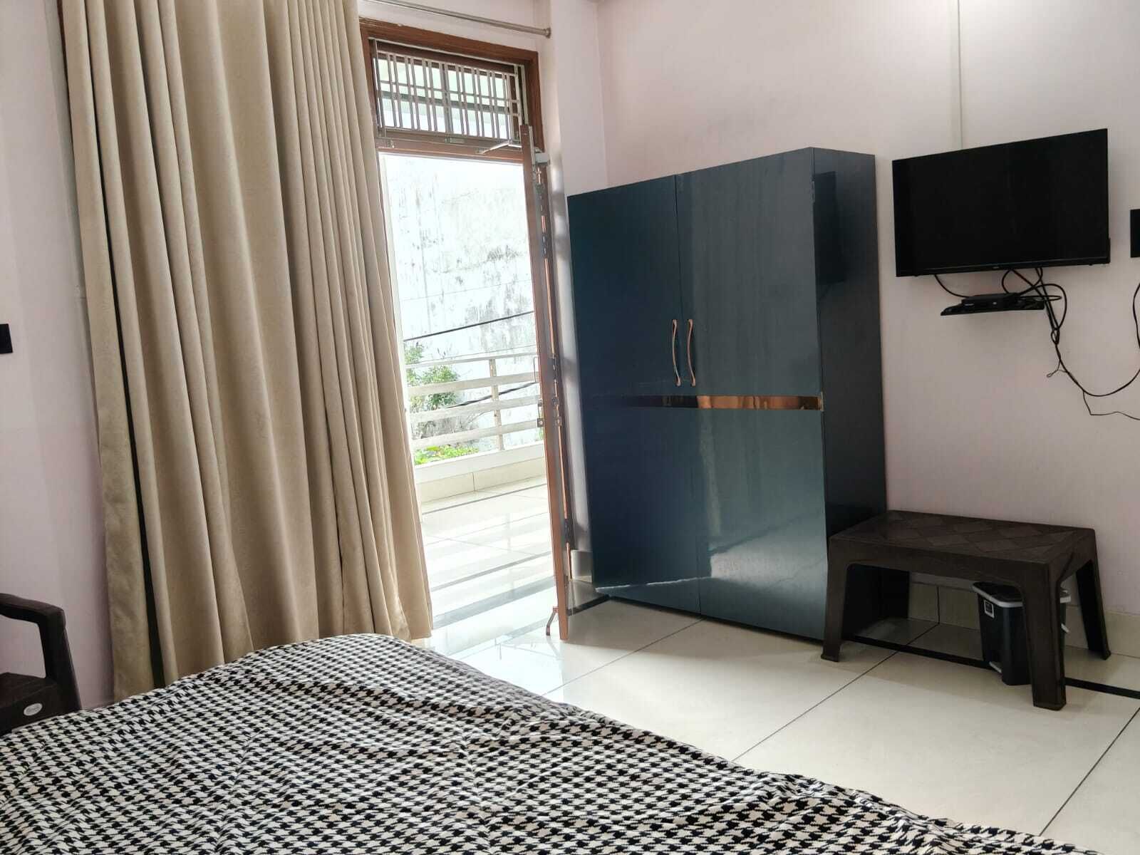 A bedroom with a bed, a wardrobe, a television, and a window with curtains.