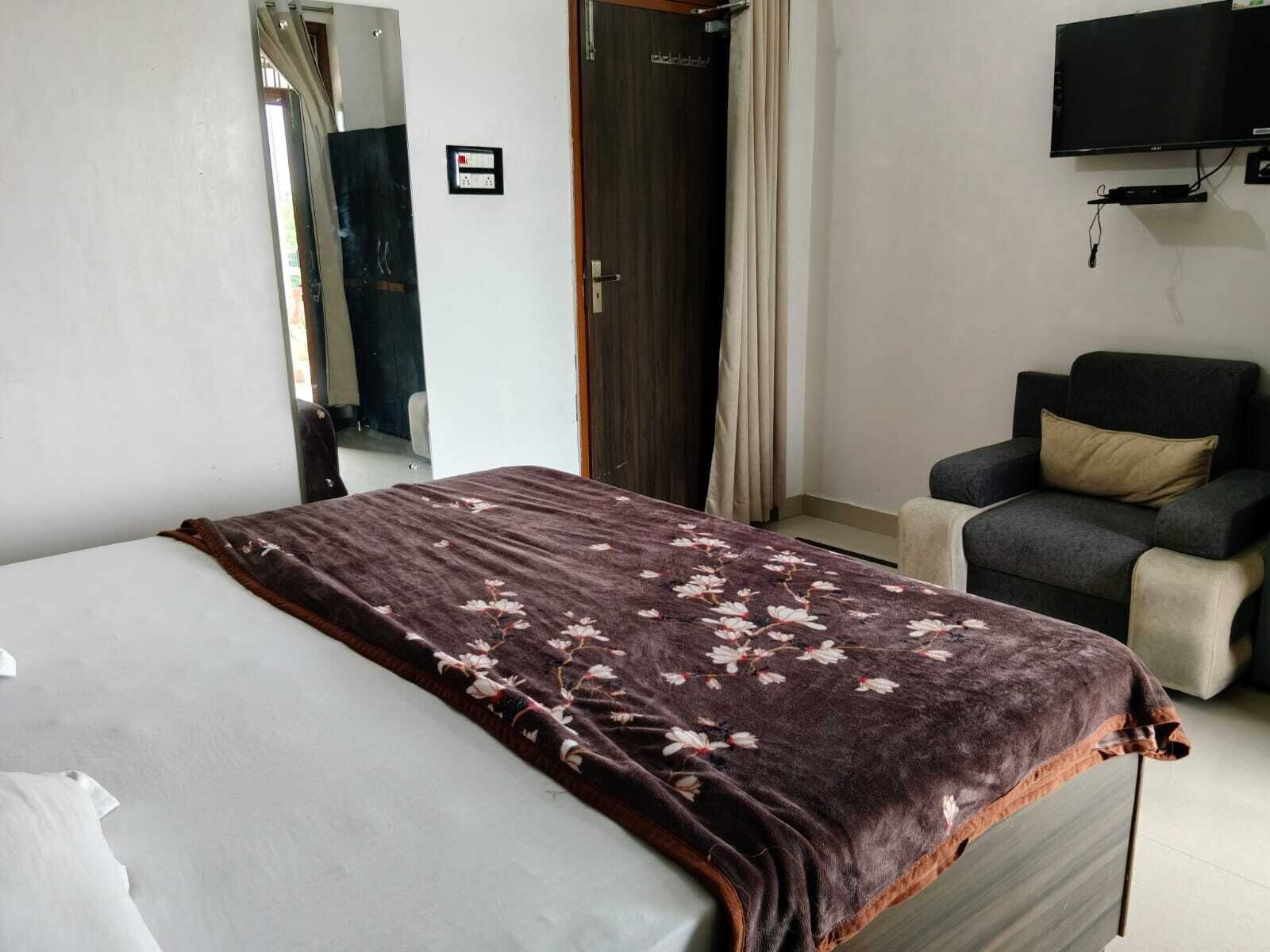 A hotel room with a bed, a chair, a television, and a door.