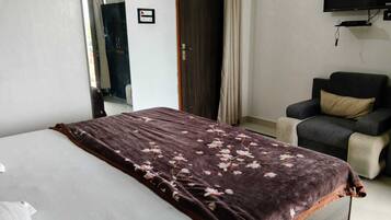 A hotel room with a bed, a chair, a television, and a door.