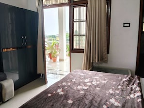 A room with a bed, a wardrobe, a balcony with potted plants, and a view of the outside. - Shri Shyam Gest House (Sultanpur)