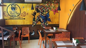 Interior de una cafetería con paredes de madera, sillas anaranjadas y un mural de una mujer con flores.