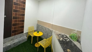 A small enclosed space with a door, two chairs, a small table, and a potted plant.