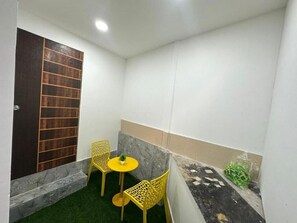 A small enclosed space with a door, two chairs, a small table, and a potted plant.