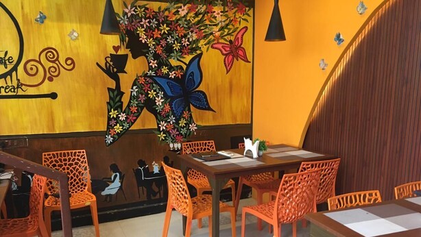 Interior de restaurante con paredes de madera, sillas naranjas, una mesa con un florero y un mural con flores y mariposas.