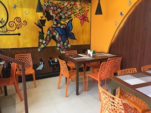 Interior de restaurante con paredes de madera, sillas naranjas, una mesa con un florero y un mural con flores y mariposas.