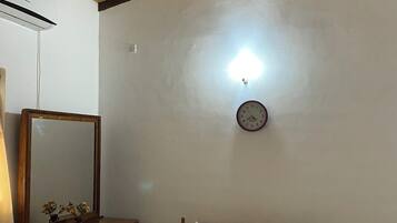 A bedroom with a wooden ceiling, a bed with a floral bedspread, a bedside table with a mirror, and a wall clock.