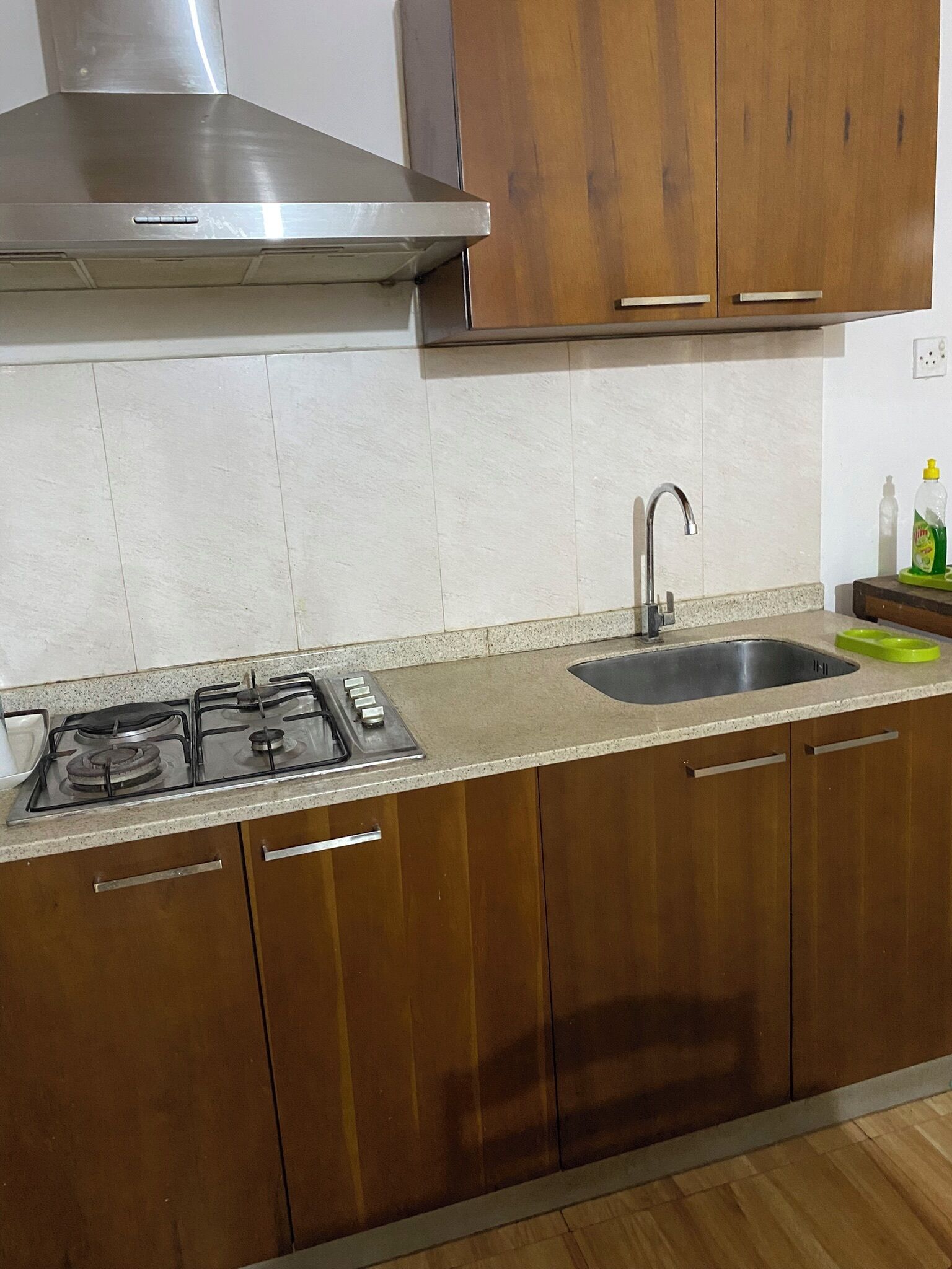 A kitchen with a gas stove, stainless steel range hood, wooden cabinets, a sink, and a countertop.