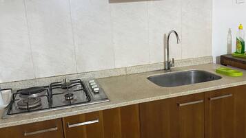 A kitchen with a gas stove, stainless steel range hood, wooden cabinets, a sink, and a countertop.