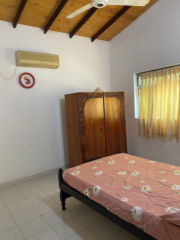 A bedroom with a bed, a wardrobe, a ceiling fan, a wall-mounted heater, and a window with curtains.