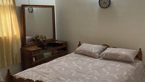 Une chambre avec un plafond en bois, un lit recouvert d’une couvre-lit à motifs floraux, une table de chevet avec un miroir et une horloge murale.