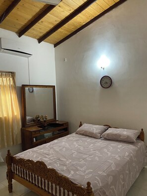 Un dormitorio con techo de madera, una cama con colcha estampada, una mesita de noche con espejo y un reloj de pared.