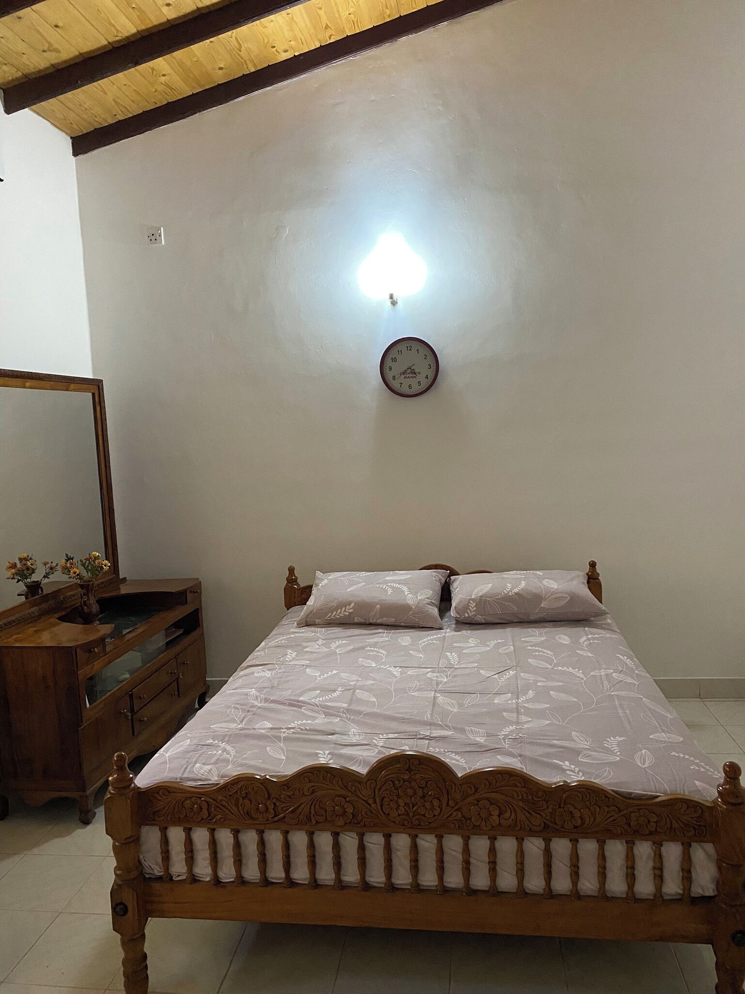 A bedroom with a wooden bed, a nightstand, a mirror, and a wall clock.
